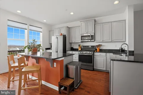 a kitchen with stainless steel appliances kitchen island granite countertop a refrigerator a stove a sink dishwasher and white cabinets with wooden floor