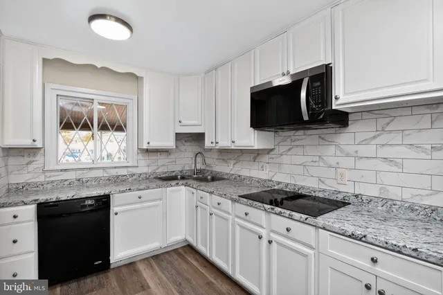a kitchen with stainless steel appliances granite countertop white cabinets a sink a stove a microwave and wooden floors