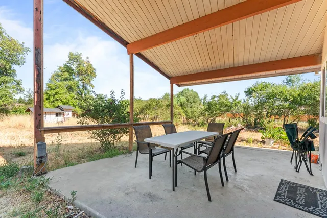 a view of a patio with table and chairs and floor to ceiling window next to a yard
