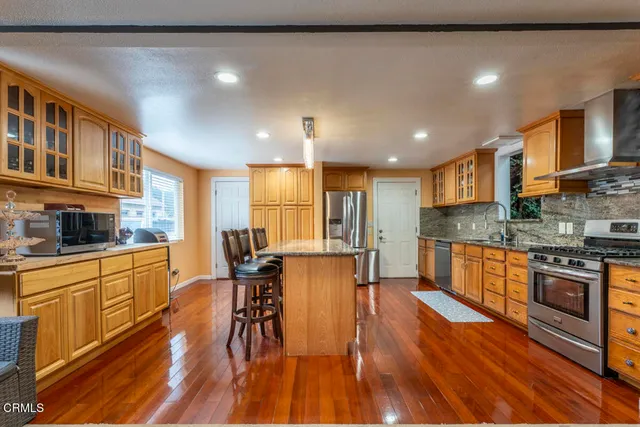 a kitchen with stainless steel appliances granite countertop a stove top oven a sink dishwasher a dining table and chairs with wooden floor