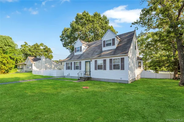 a house that is sitting in the grass with large trees and plants