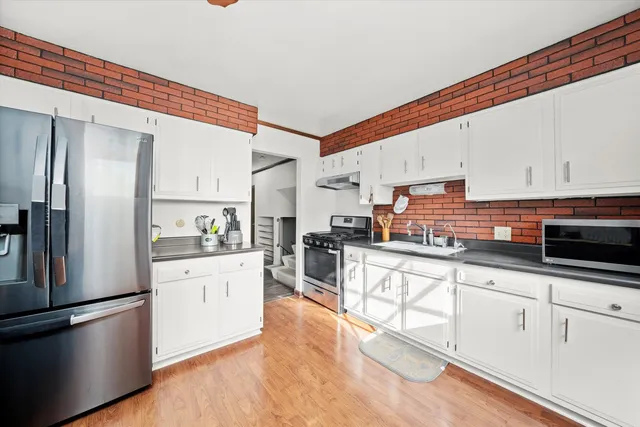 a kitchen with stainless steel appliances kitchen island granite countertop a refrigerator a stove a sink and white cabinets with wooden floor