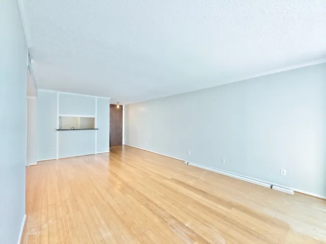 a view of empty room with wooden floor and kitchen
