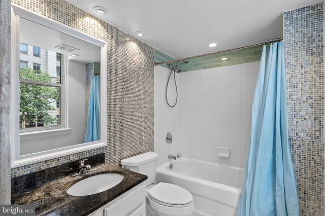 a bathroom with a granite countertop sink toilet a shower a mirror and a tub