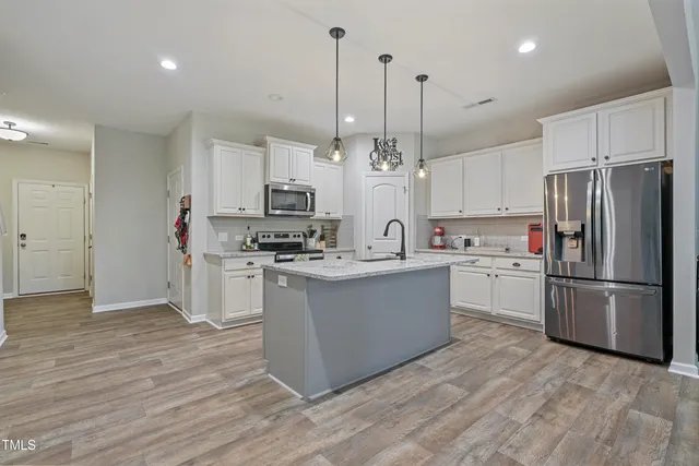 a kitchen with stainless steel appliances kitchen island granite countertop a refrigerator a sink dishwasher a stove and white cabinets with wooden floor