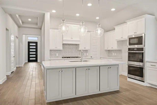 a large kitchen with stainless steel appliances granite countertop a large kitchen island a stove a sink a refrigerator and white cabinets with wooden floor
