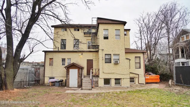 a view of a white house with a large tree and wooden fence