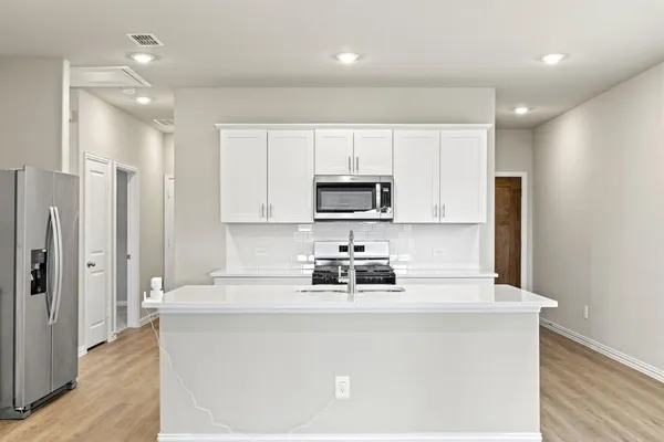 a kitchen with stainless steel appliances a refrigerator a stove a sink and white cabinets
