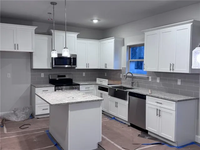 a kitchen with kitchen island granite countertop stainless steel appliances a sink a stove a microwave a center island and cabinets