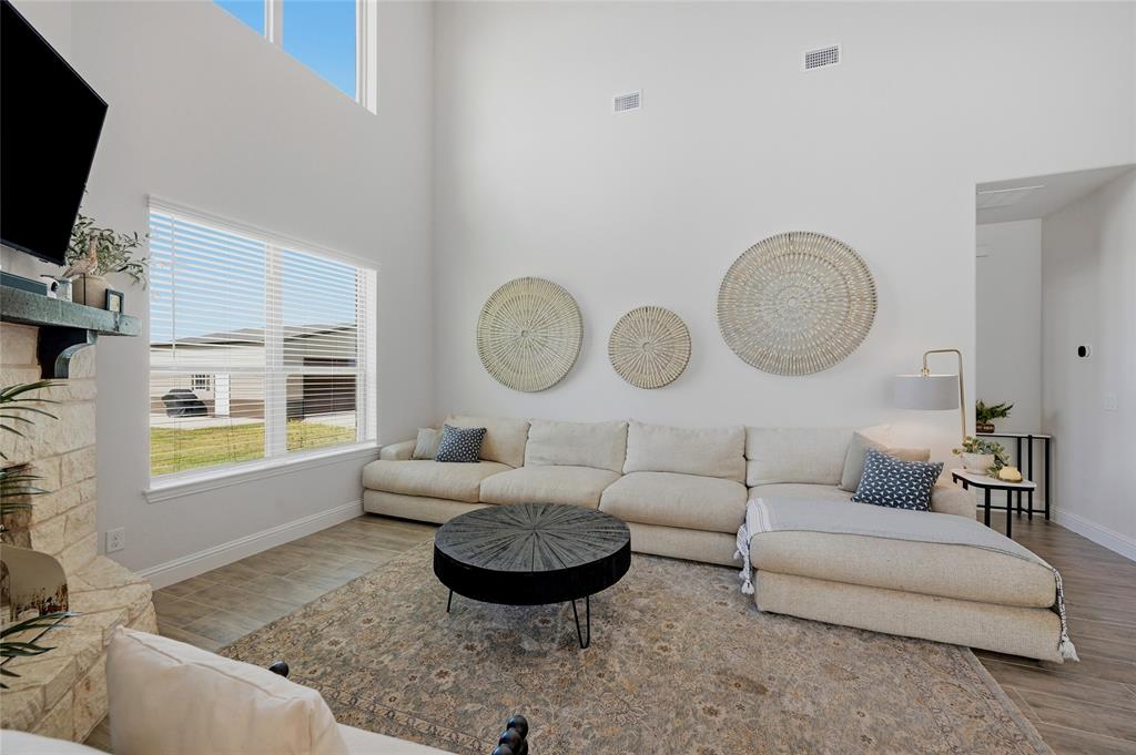 864 Shadow Valley Road Whitesboro, TX 76273 - Photo 19 of 40 Vaulted ceiling living area featuring a stone-clad fireplace, a large rectangular window, and high-set windows