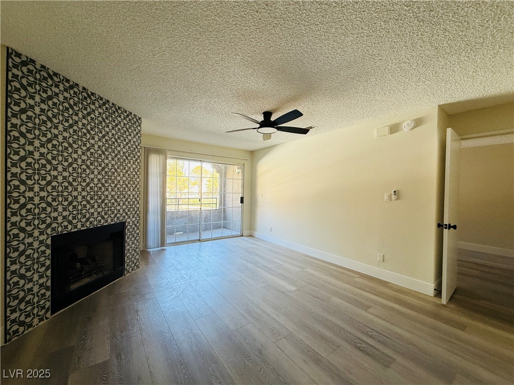 2200 South Fort Apache Road, Unit 2095 Las Vegas, NV 89117 - Photo 4 of 16 Unfurnished living room featuring a textured ceiling, a fireplace, light wood-style floors, and a ceiling fan