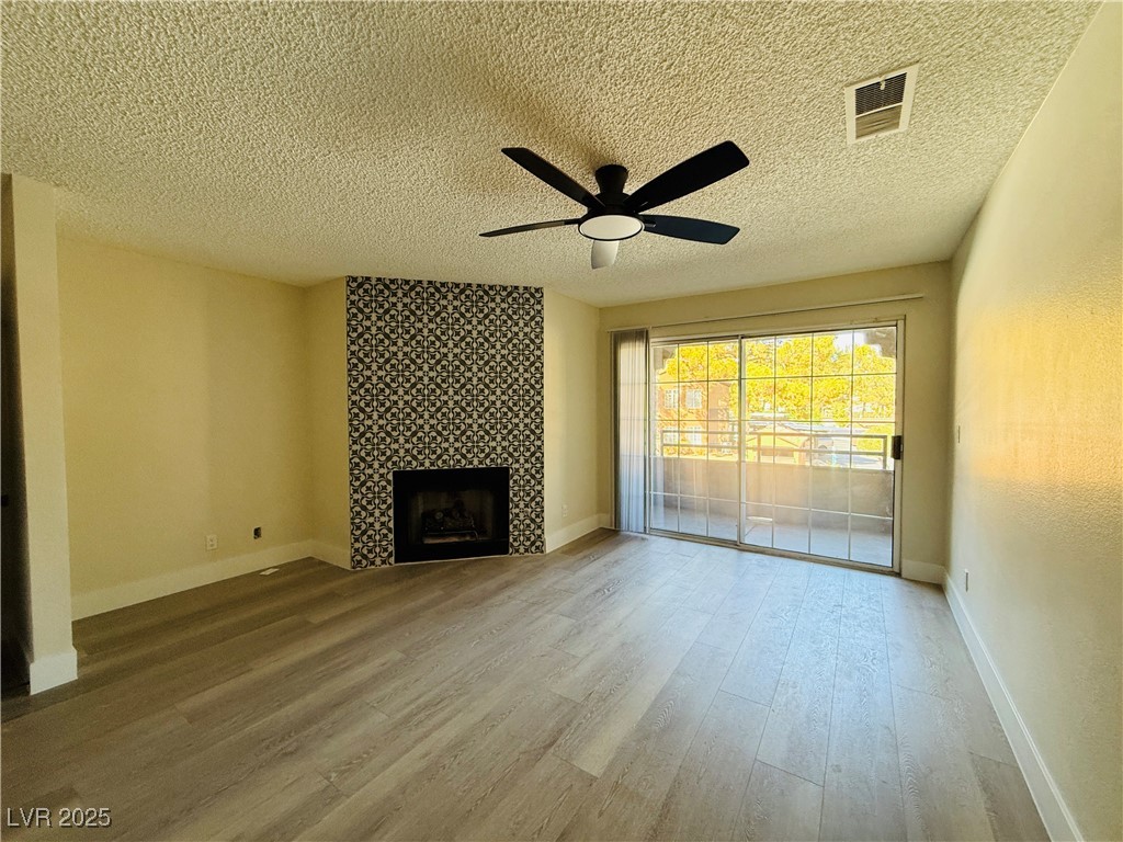 2200 South Fort Apache Road, Unit 2095 Las Vegas, NV 89117 - Photo 5 of 16 Unfurnished living room featuring light wood-style flooring, a textured ceiling, a tiled fireplace, and a ceiling fan