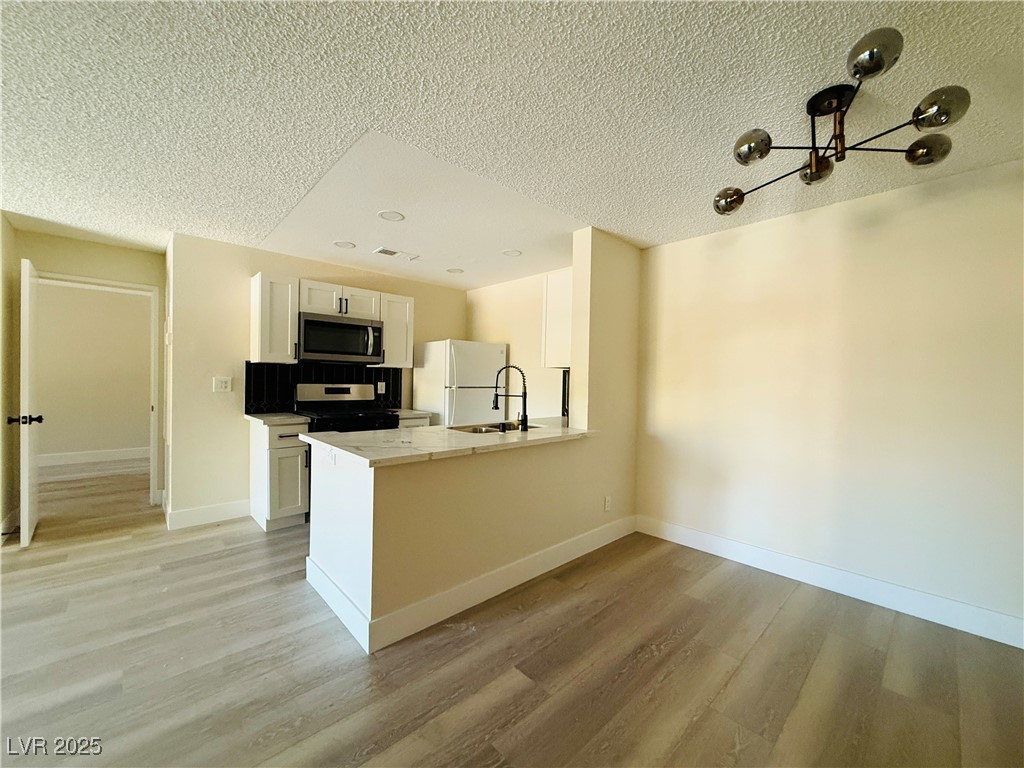 2200 South Fort Apache Road, Unit 2095 Las Vegas, NV 89117 - Photo 8 of 16 Kitchen with light countertops, light wood finished floors, a peninsula, black stove, and stainless steel microwave