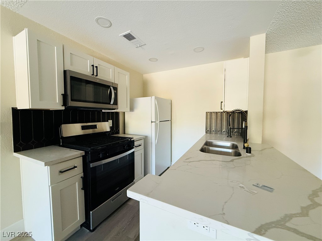 2200 South Fort Apache Road, Unit 2095 Las Vegas, NV 89117 - Photo 9 of 16 Kitchen with gas range oven, stainless steel microwave, light stone counters, white cabinetry, and freestanding refrigerator