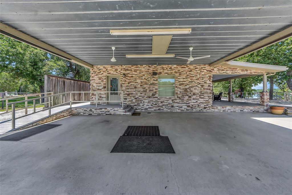 566 Selma Park Road Bowie, TX 76230 - Photo 20 of 40 Covered concrete parking area featuring a stone veneer exterior wall, a glass-paned entry door, and a window with blinds