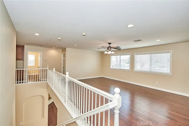 an empty room with wooden floor windows and a ceiling fan