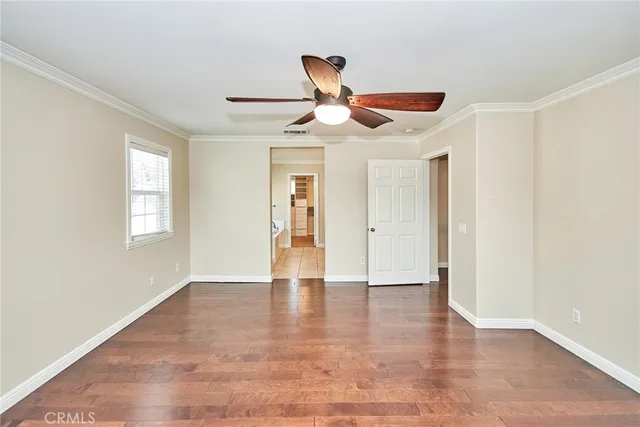 a view of an empty room with wooden floor and a ceiling fan