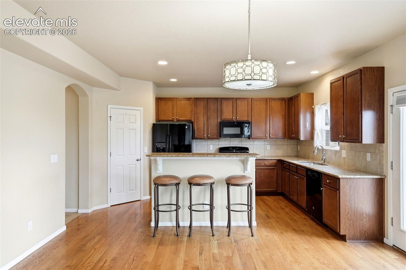 7274 Red Cardinal Loop Colorado Springs, CO 80908 - Photo 8 of 33 Full kitchen featuring wood-finish flooring, dark wood cabinetry, a breakfast bar, and a tile backsplash