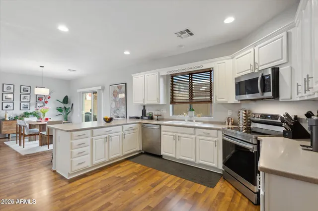 a kitchen with stainless steel appliances granite countertop a stove top oven a sink dishwasher a dining table and chairs with wooden floor