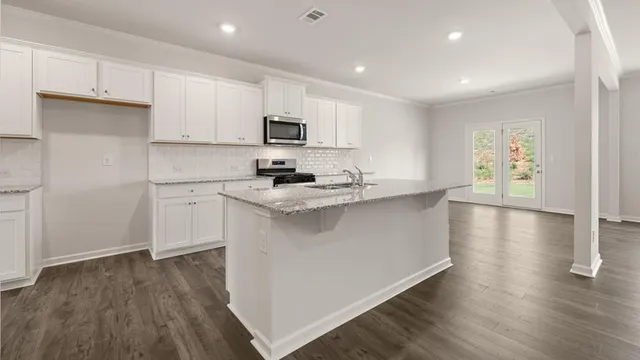a kitchen with stainless steel appliances a sink a stove top oven a wooden floor and cabinets