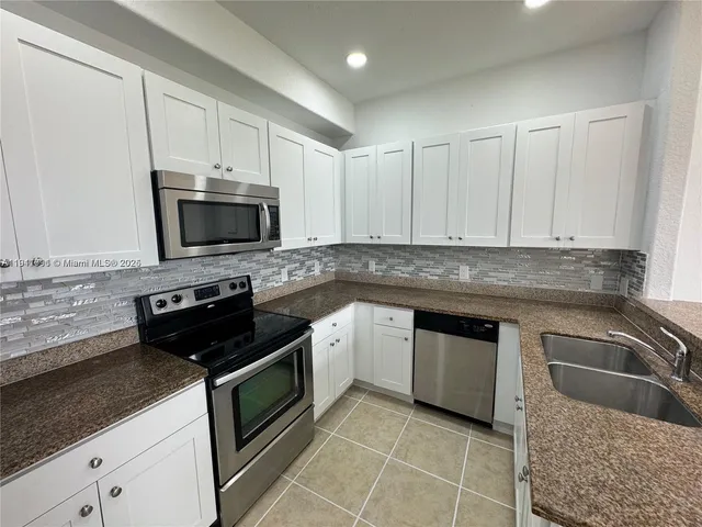 a kitchen with granite countertop a sink dishwasher stove and cabinets