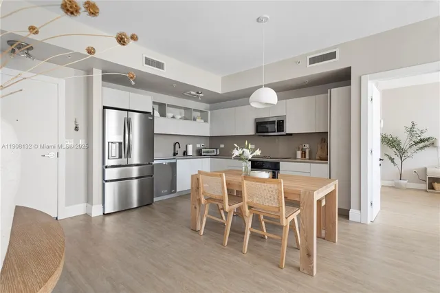 a kitchen with stainless steel appliances kitchen island granite countertop a refrigerator a stove a microwave oven a dining table and chairs with wooden floor