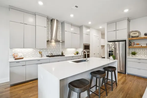 a kitchen with stainless steel appliances granite countertop a sink a stove a refrigerator and white cabinets with wooden floor