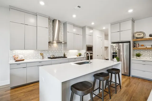 a kitchen with stainless steel appliances granite countertop a sink a stove a refrigerator and white cabinets with wooden floor