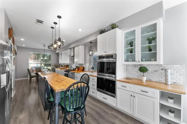 a kitchen with stainless steel appliances a dining table chairs a sink dishwasher a refrigerator and microwave with wooden floor