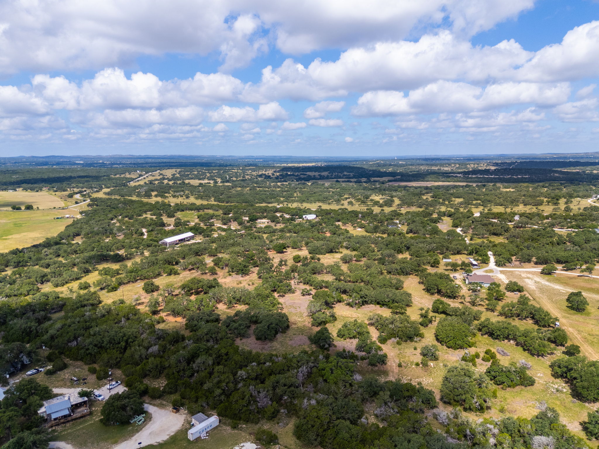 5385 Ranch Road 165 Blanco, TX 78606 - Photo 31 of 40 An aerial perspective reveals vast acreage with scattered trees and distant structures under a clear sky.