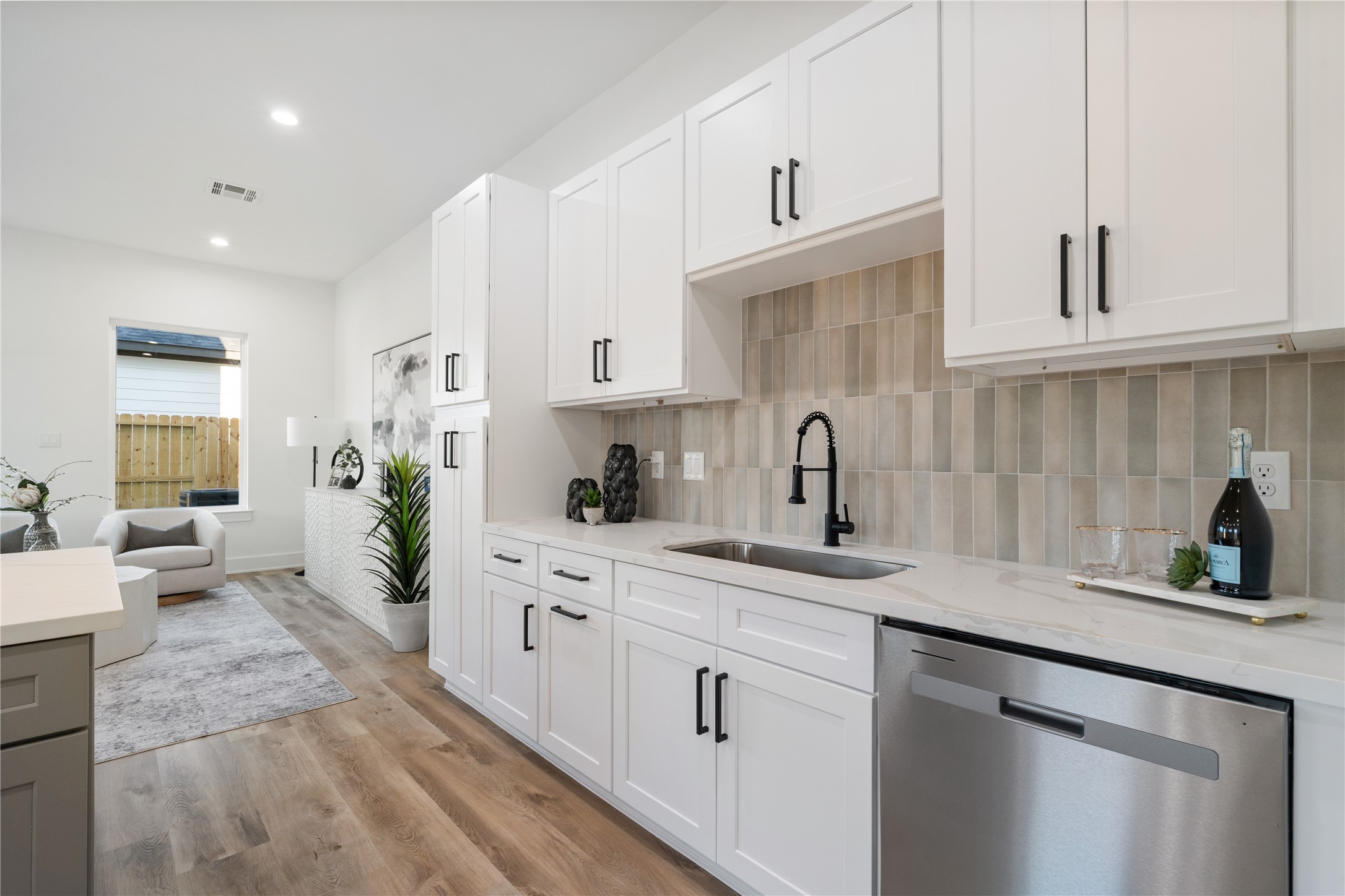9003 Comal Street Houston, TX 77051 - Photo 9 of 36 The undermount farmhouse-style sink is tucked to the side, surrounded by ample soft-close cabinetry for generous storage. A striking backsplash in a mix of light green and earthy brown tones adds warmth and character to the space. This thoughtful design perfectly balances functionality with modern farmhouse charm