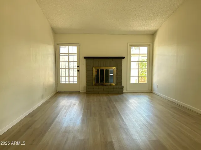 an empty room with wooden floor fireplace and windows