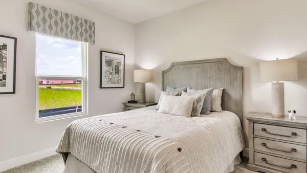 a bedroom with a bed and a lamp on dresser next to a window