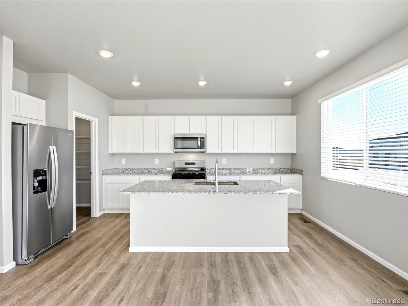 7317 West 27th St Road Greeley, CO 80634 - Photo 7 of 28 a large kitchen with stainless steel appliances a large white kitchen island a refrigerator a stove a sink and a microwave