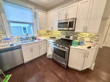 a white kitchen with wooden floor and stainless steel appliances