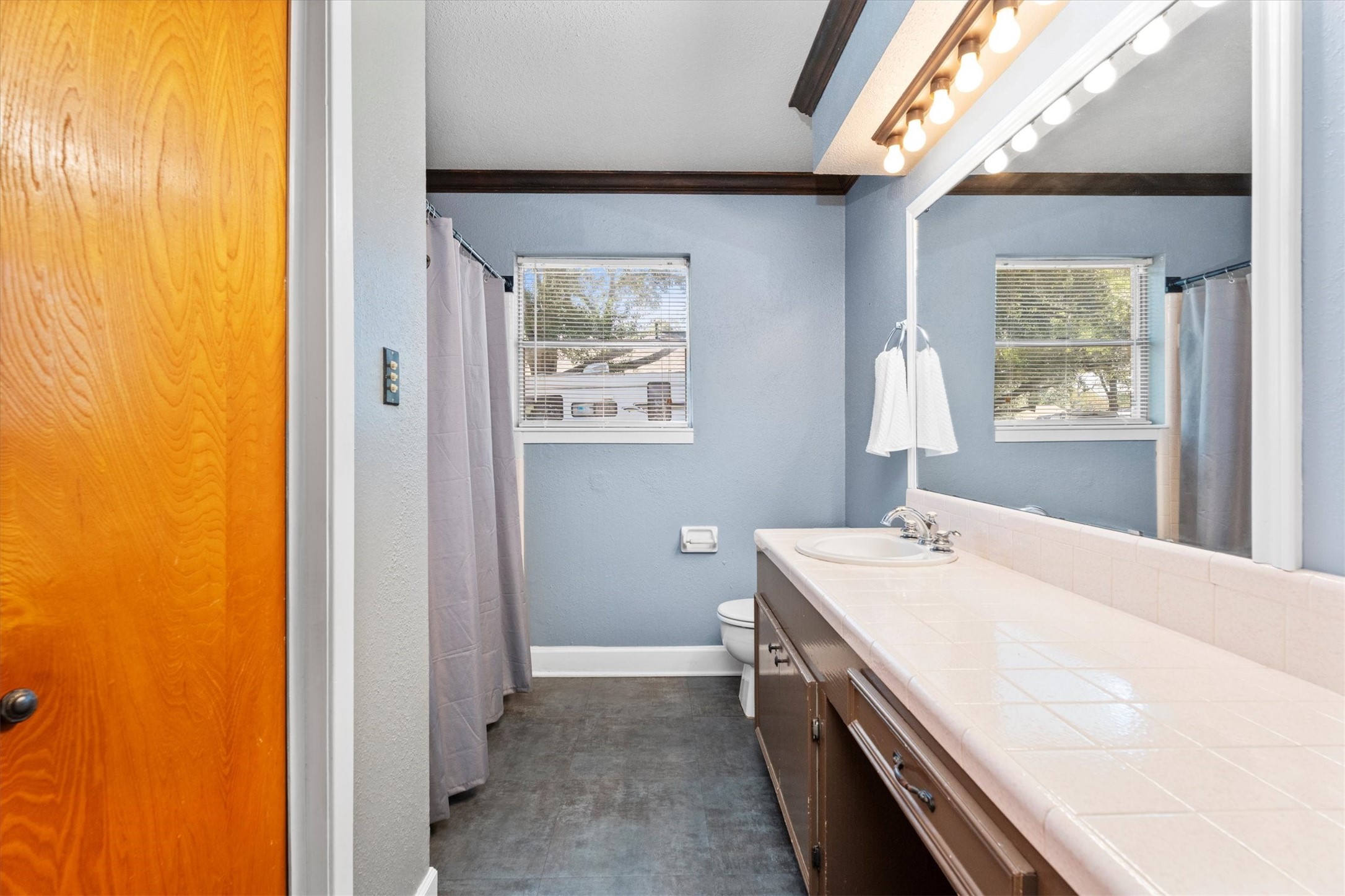104 Anna Street Tomball, TX 77375 - Photo 13 of 32 The one bathroom in the house sits between the first and second bedrooms on the left side of the house. It features a long vanity with ample counter space, a large mirror with bright lighting, and a neutral color scheme. It includes a shower/tub combo, extra closet space and cabinetry for linens/supplies and a windows for natural light.