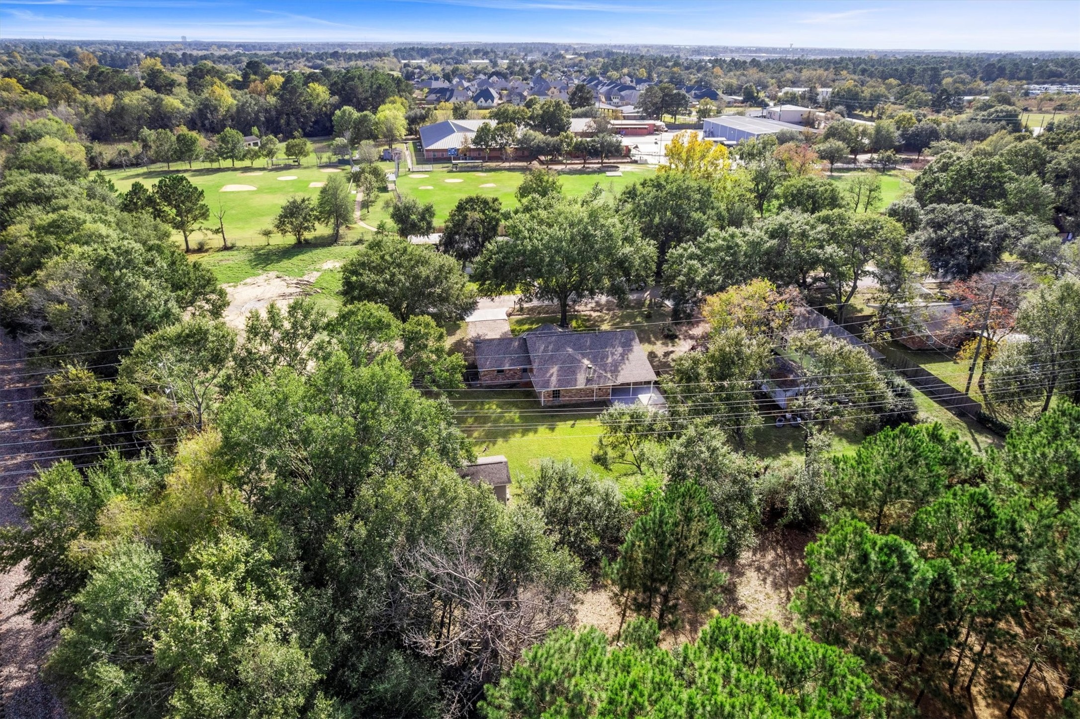 104 Anna Street Tomball, TX 77375 - Photo 27 of 32 This aerial photo showcases a serene residential area with lush greenery and mature trees. This is the view from behind the lot looking south. Behind the house across the street, there is a church that has a couple of ball fields. They also own the land at the end of Anna Street.