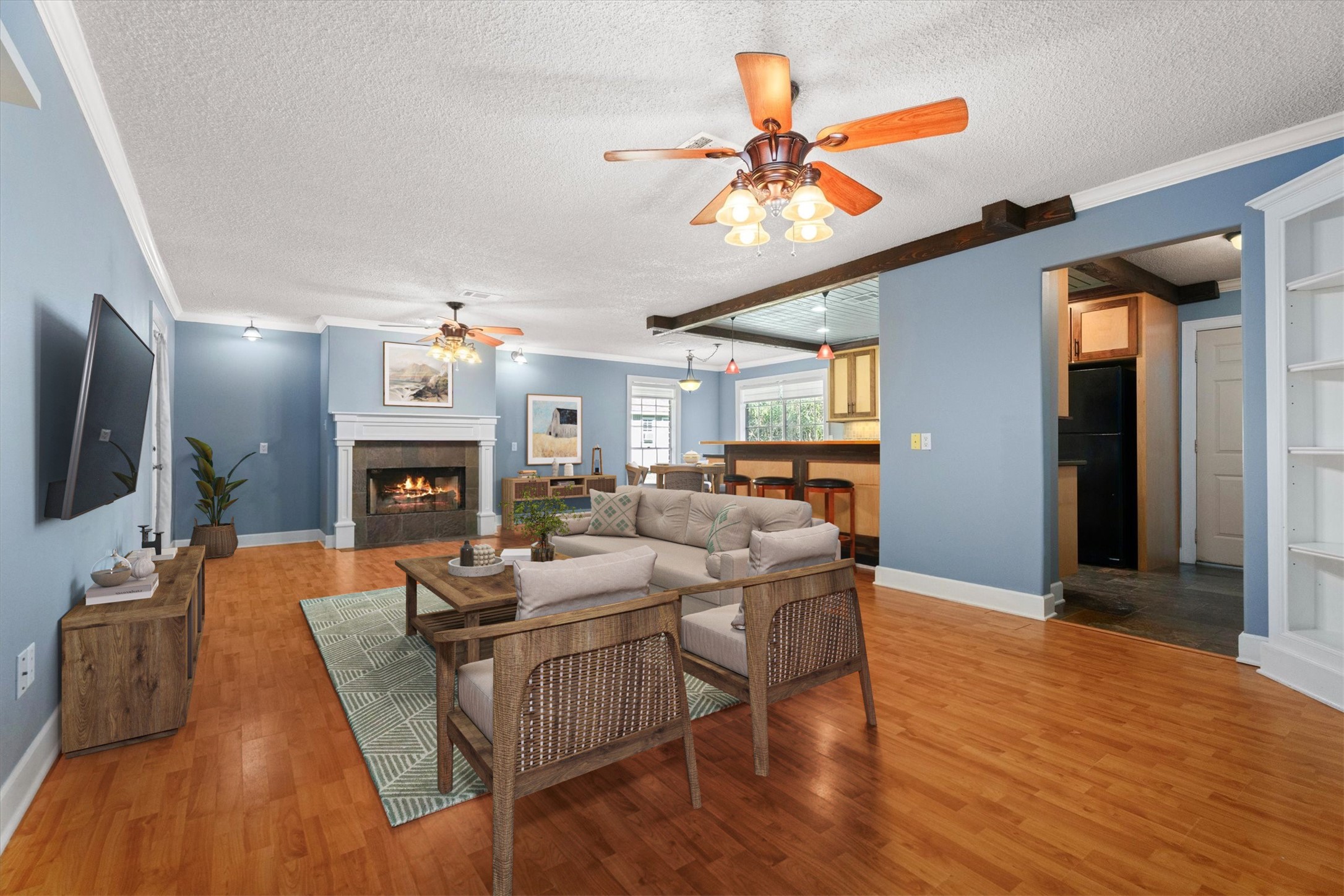 104 Anna Street Tomball, TX 77375 - Photo 3 of 32 This spacious living area features warm wood flooring, a cozy fireplace, and a ceiling fan. The open layout connects to the kitchen, complete with a breakfast bar and modern lighting. Ample natural light and built-in shelving enhance the inviting atmosphere. Virtually Staged.