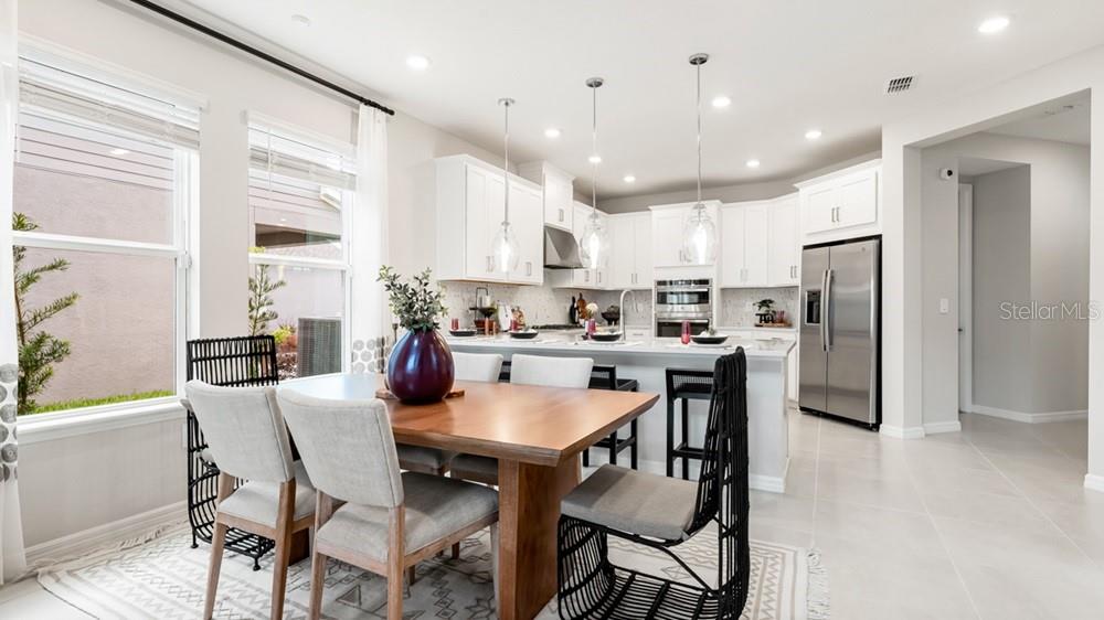13505 Commons Avenue Parrish, FL 34219 - Photo 12 of 26 a kitchen with stainless steel appliances kitchen island granite countertop a dining table chairs refrigerator and sink