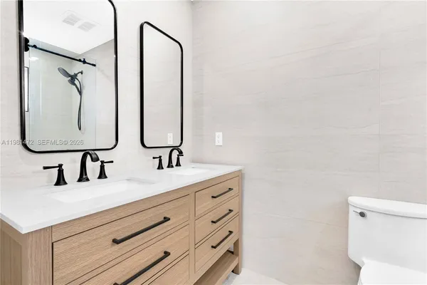 a bathroom with a double vanity sink and mirror with toilet