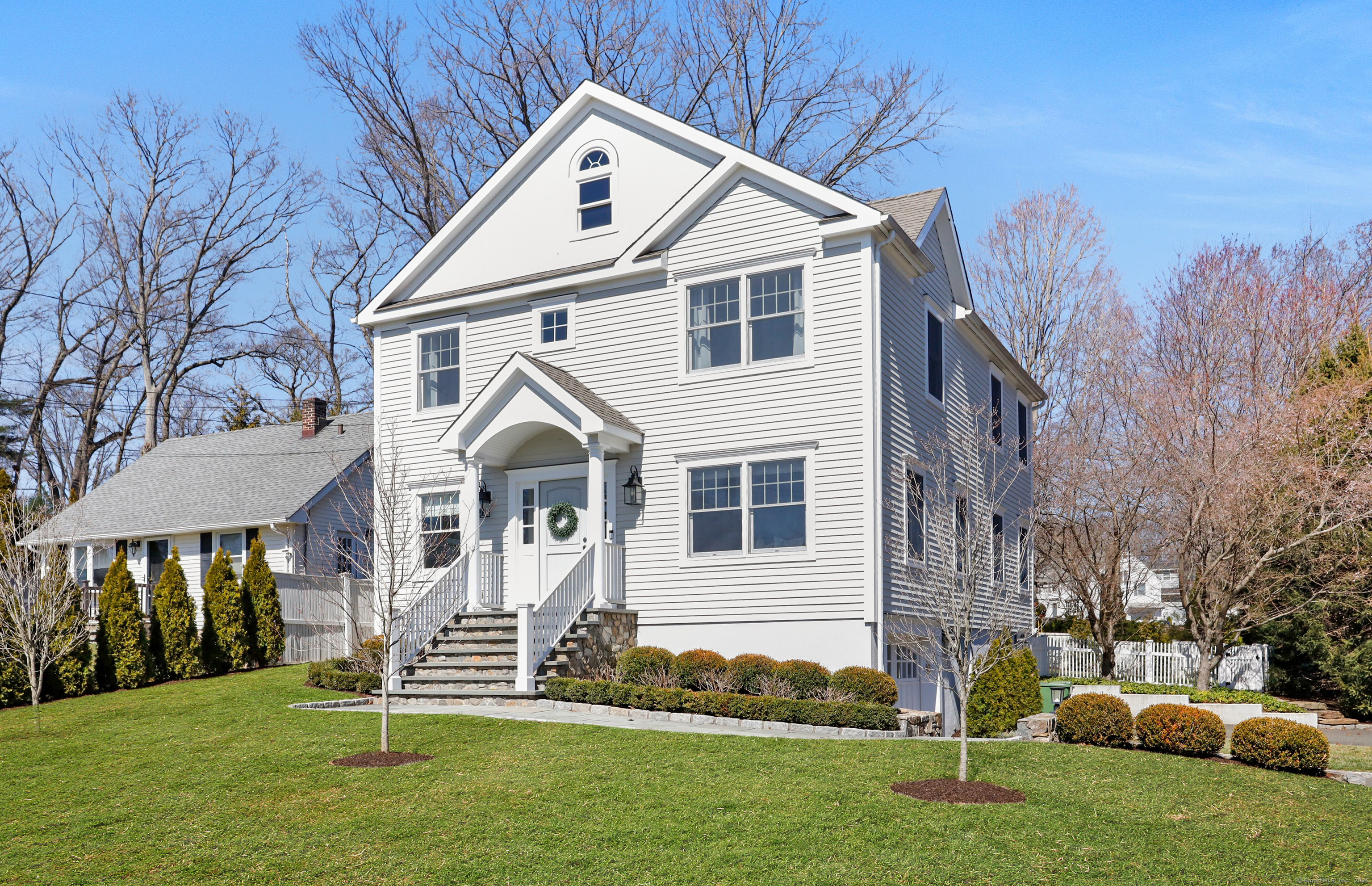 a view of a white house next to a yard with big trees