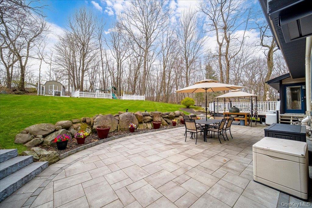 157 Brewer Road Newburgh, NY 12550 - Photo 41 of 50 Expansive paved patio with outdoor dining area, retaining wall, and a sloped lawn with mature trees