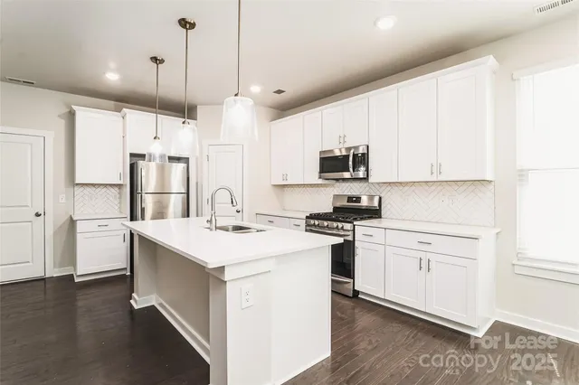 a kitchen with stainless steel appliances granite countertop a sink a stove a refrigerator and white cabinets with wooden floor