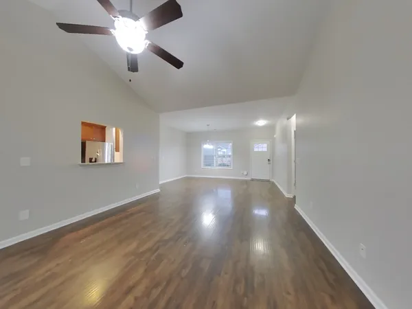 a view of an empty room with wooden floor and a ceiling fan