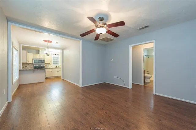 a view of an empty room and kitchen with wooden floor