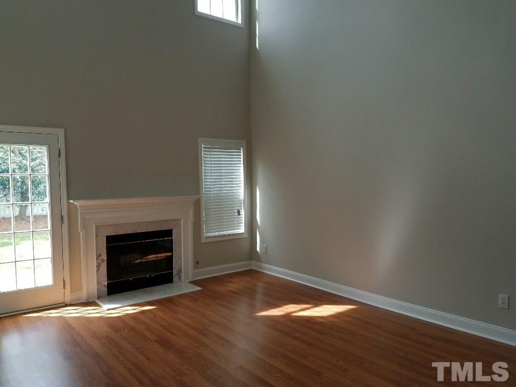 5021 Village Lawn Drive Raleigh, NC 27613 - Photo 3 of 9 an empty room with wooden floor fireplace and windows