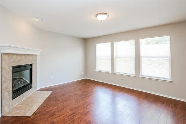 an empty room with wooden floor fireplace and windows