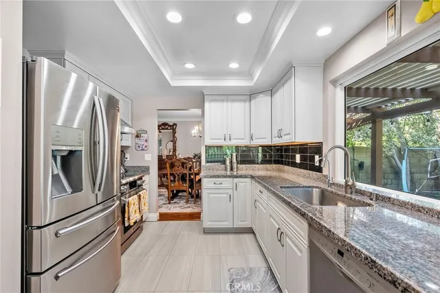 a kitchen with stainless steel appliances granite countertop a refrigerator a sink dishwasher a stove and white countertops with wooden floor