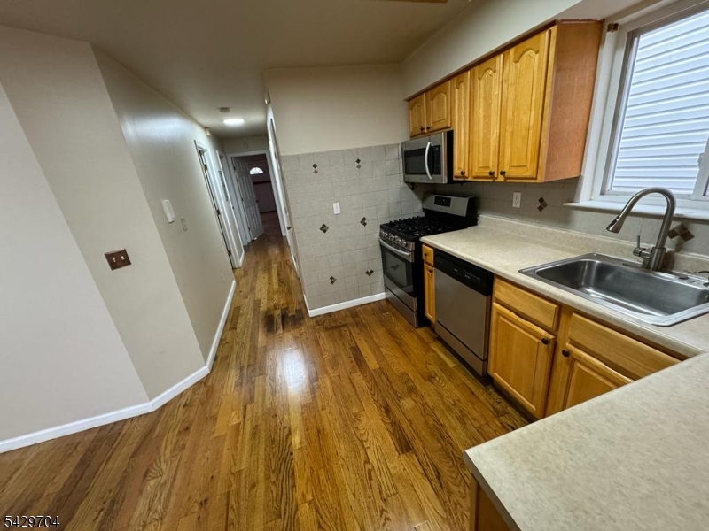 821 Anna Street Elizabeth, NJ 07201 - Photo 10 of 11 a kitchen with wooden floors wooden cabinets a sink a window and stainless steel appliances