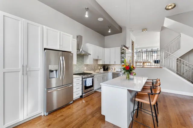 a kitchen with stainless steel appliances a refrigerator a stove a sink dishwasher and white cabinets with wooden floor